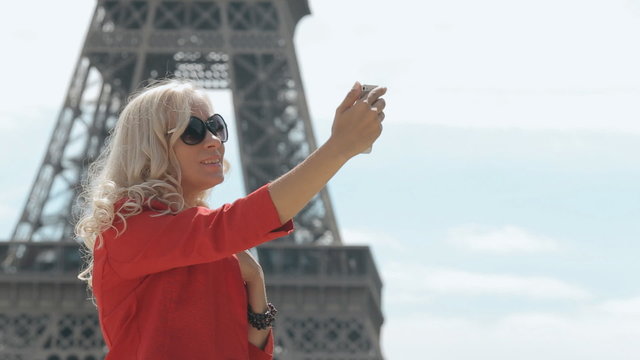 Attractive blonde in sunglasses doing selfie against the backdrop of the Eiffel Tower in Paris