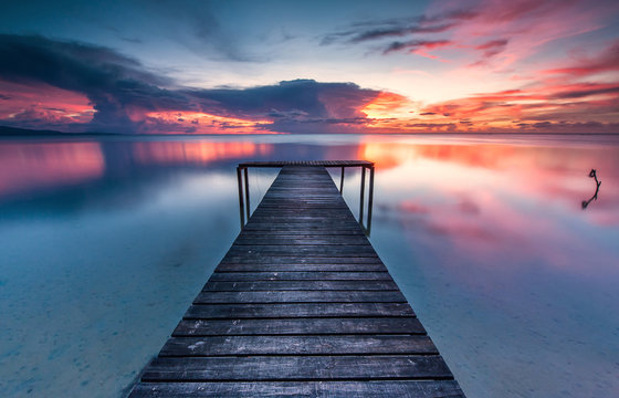 Fototapeta romantic sunset colour with reflection and wooden jetty as foreground