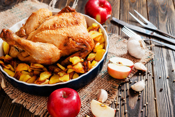 
Baked chicken with baked potatoes , apples , garlic and spices on a wooden background