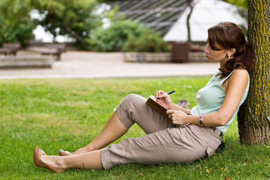 Young attractive fresh woman at the park writes in notebook jour