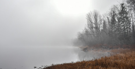 Obraz na płótnie Canvas Dense fog envelopes Ottawa River and shoreline - obscured sunshine through fog, bright diffusion, mid-morning sunrise.