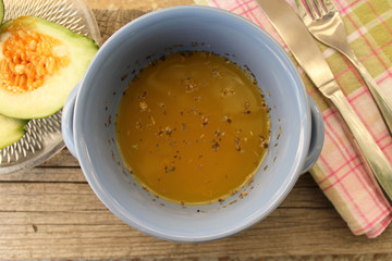 Pumpkin yellow soup in blue dish, slice of pumpkin on plaid table cloth, spoon and fork 