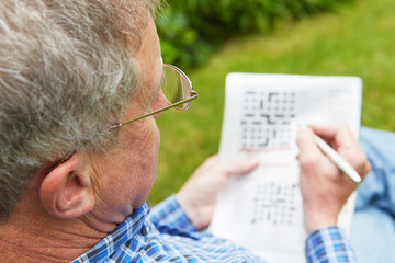 Naklejka premium Senior Man Doing Crossword Puzzle In Garden