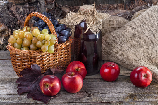 Black and white grapes with red apples and fresh juice on rustic table and in front of the wood
