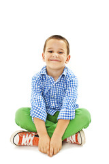 Smiling little boy sitting down on floor and looking at camera. Isolated on white background 
