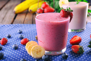 Glasses of fresh cold smoothie with fruit and berries, on blue tablecloth background