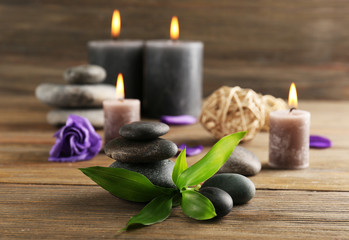 Fototapeta na wymiar Relax set contains alight wax candles with flowers and pebbles on wooden background, focus on green leaf