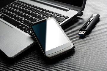 Blank Black Smartphone With Blue Reflection Leaning On A Notebook Keyboard Next To A Plugged In USB...