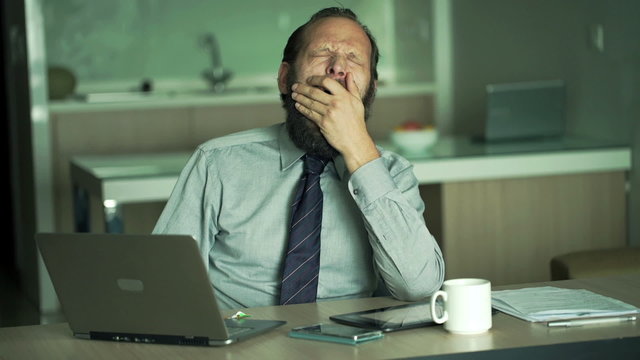 Tired businessman with laptop falling asleep in office 
