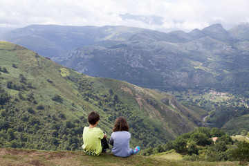 Fototapeta na wymiar Niños sentados sobre la hierba contemplando las montañas