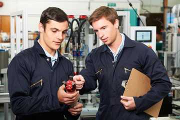 Engineer And Trainee Discussing Component In Factory