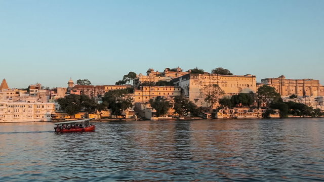 Tourist boat passing in front of Udaipur City Palace, view  from Lake Pichola on sunset. Udaipur, India