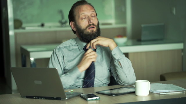 Sad, tired businessman working with laptop in office
