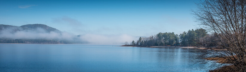 Panoramic view of fog lifting off the Ottawa River in the morning, blue sky, clear bright day with Laurentian hills.