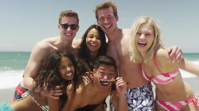 Portrait of young group of friends on the beach smiling at camera 
