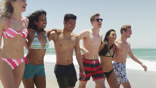 Happy young group of interracial friends skipping on the beach