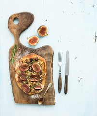 Rustic homemade pizza with figs, prosciutto and mozzarella cheese on dark wooden serving board over...