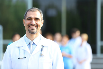 Happy doctor with medical stuff behind standing against clinic entrance