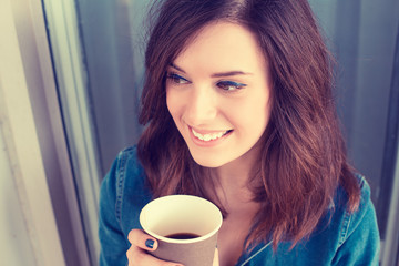 Smiling woman drinking coffee outdoors holding paper cup