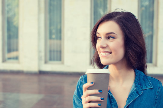 Smiling woman drinking coffee outdoors holding paper cup