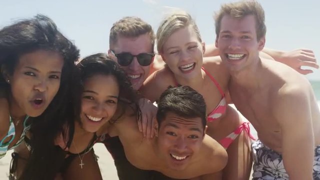 Group portrait of young interracial friends huddled enjoying the beach