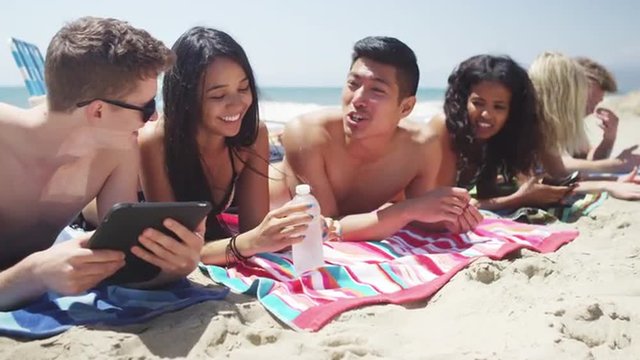 Portrait of young adult interracial friends lying talking on the beach close up
