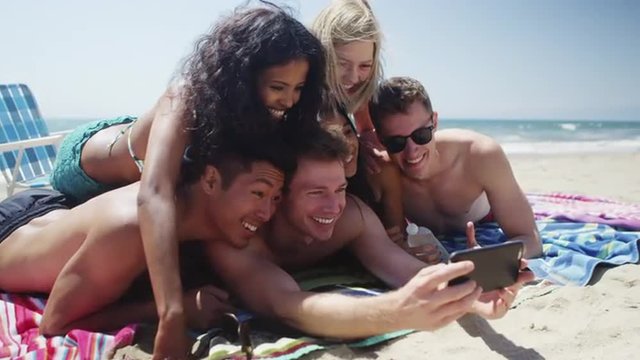 Young adult group of multi ethnic friends lying on sand taking selfie