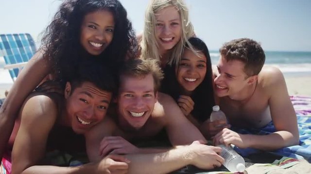 Portrait of group of young multi ethnic friends smiling into camera on the beach