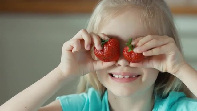 Laughing girl playing with two strawberries. Closeup portrait