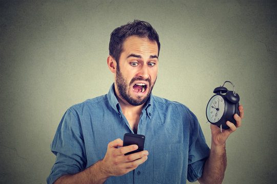 surprised business man with alarm clock looking at smart phone