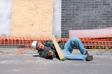 A fallen and injured construction worker in a hard hat laying on the ground at a construction work site