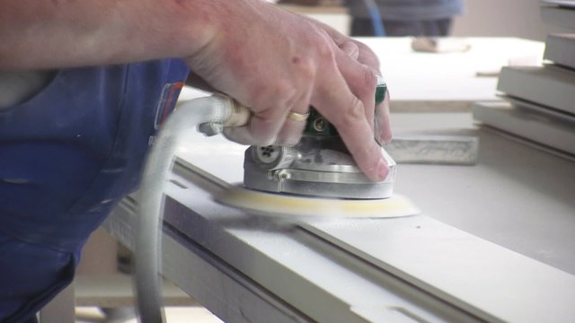 Worker using a power sander to smooth part of the doors frame.
