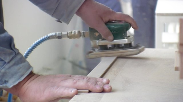 Worker using a power sander to smooth part of the doors frame.

