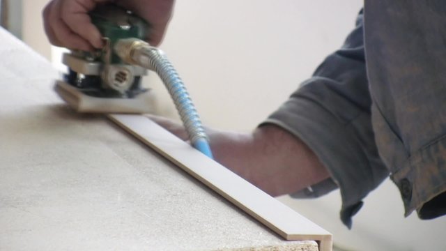 Worker using a power sander to smooth part of the doors frame.
