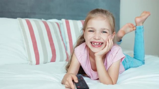 Laughing girl watching TV. Child lying on the bed. Child shocked TV