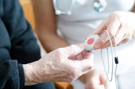 Pflegekraft überreicht älterer Dame einen Notfallknopf