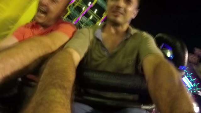 Slow motion of excited people on the roller coaster ride in amusement park at night.