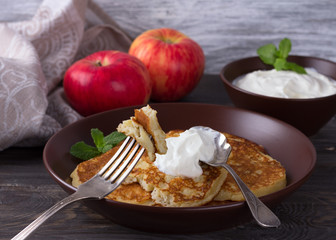 Cottage cheese pancake with apples in ceramic bowl with sour cream on a dark wooden table