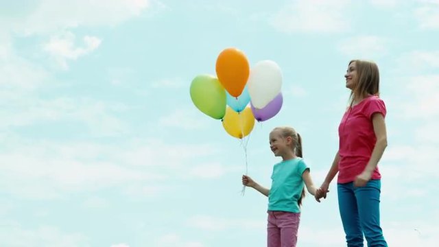 Mother and daughter with balloons looking at camera. Child holding balloons