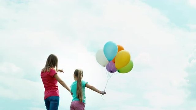 Mother and daughter with balloons turned and looking at the camera. Mother and daughter holding hands and looking at distance