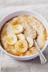 Bowl of oatmeal porridge with banana and caramel sauce on rustic table, hot and healthy breakfast every day, diet food