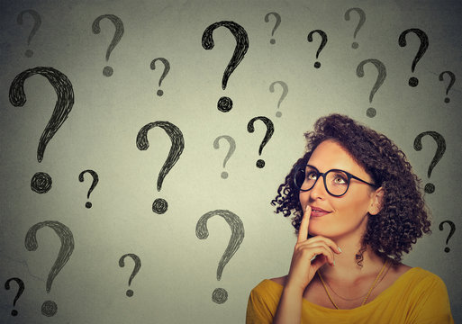 Thinking young business woman in glasses looking up at many question marks