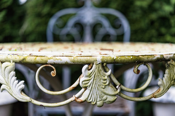 Closeup of antic rusted iron table and chair with ornaments in garden. Vintage shabby design for outdoor area, perfect for garden, lifestyle and decoration blogs, business and magazines - 96235359