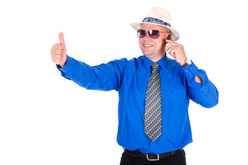 Successful and smiling businessman in blue shirt, tie, sunglasses and white hat. Speaking by cell mobile phone and shows the thumb up. Isolated white background, Concept of leadership