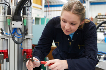 Female Apprentice Engineer Working On Machine In Factory