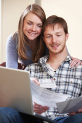 Happy Young Couple Looking At Finances On Laptop