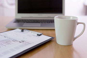 cup of coffee and laptop with document on office desk