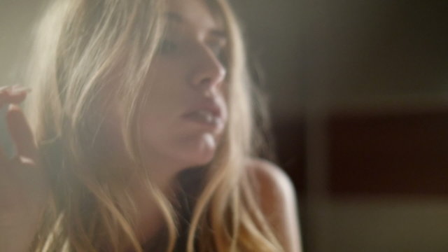 Beautiful white blond woman lying in bed, looking at camera during night time photoshoot. Gimbal camera movement slow motion shot going in and out of focus.
