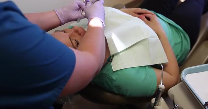 Patient Teeth Cleaning Over the Shoulder Move Right. camera moves right over the shoulder of the dentist preforming a teeth cleaning on a female patient.
