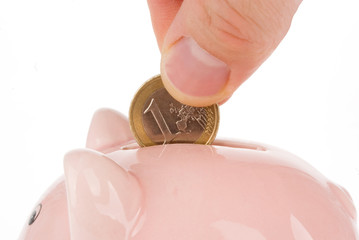 Hand putting one euro coin into piggy bank isolated on white
